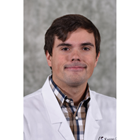 Tanner Movick smiles in his white coat in front of a gray background. 